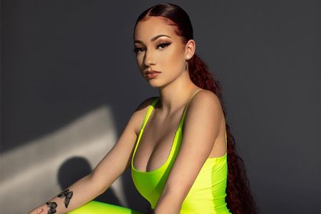 bergoli in a neon body suit, sleek back red hair and nide makeup 